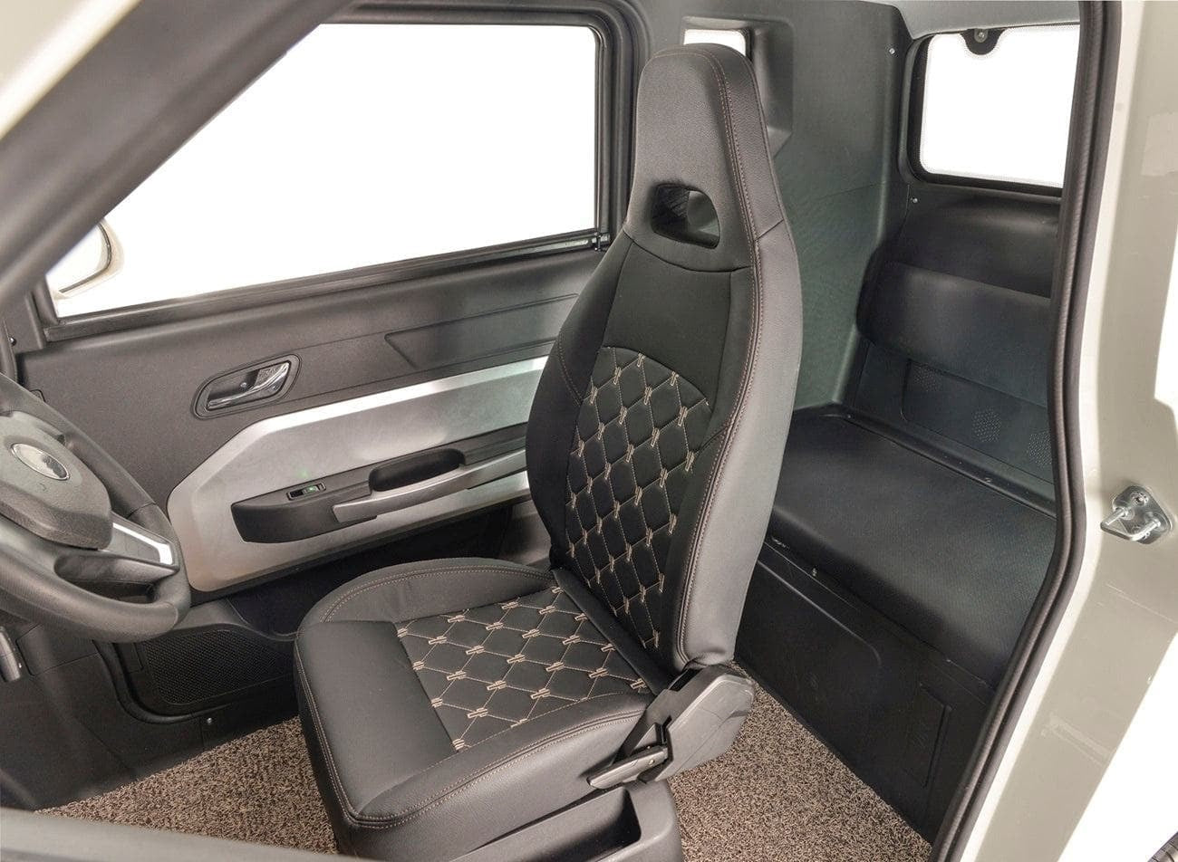 A glimpse inside the Eclipse EV Nova showcases a single black quilted driver's seat adorned with diamond-shaped stitching, accompanied by a steering wheel and minimalist design elements. The comfortable seat comes equipped with a seatbelt, and the open car door reveals an elegantly simple interior design.