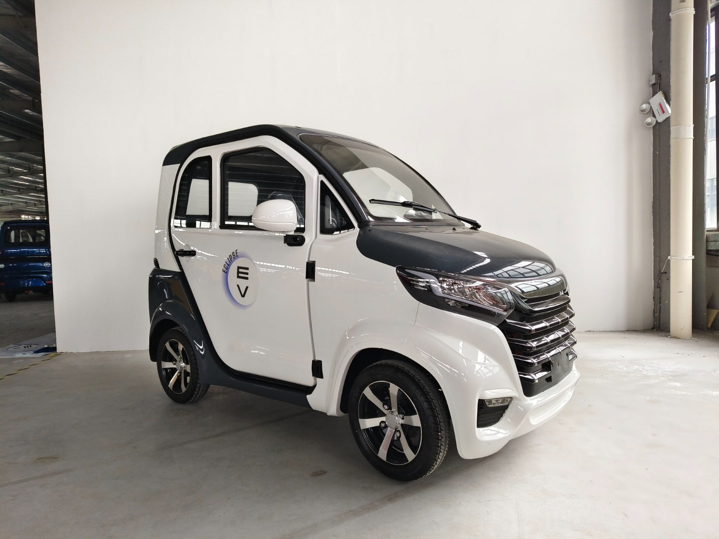 A compact white enclosed scooter with black trim, parked indoors, featuring a prominent "Eclipse EV" logo on its door and equipped with stylish black wheels.